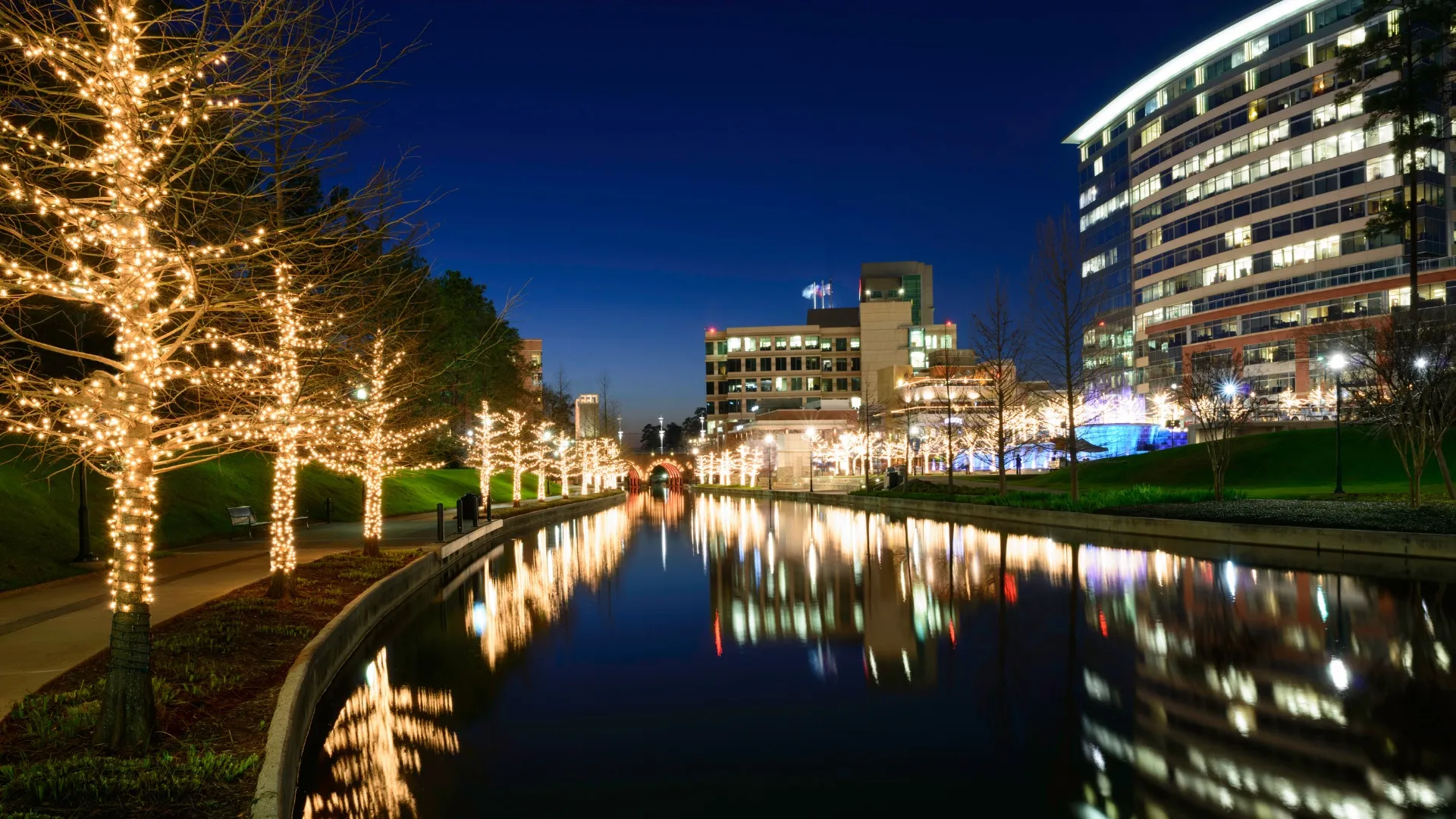 The Woodlands Waterway lit up with holiday lights at night, reflecting in the water